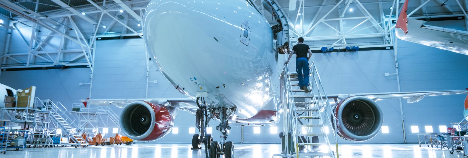 Brand New Airplane Standing in a Aircraft Maintenance Hangar while Aircraft Maintenance Engineer/ Technician/ Mechanic goes inside Cabin via Ladder/ Ramp.